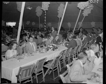 Large group of people eating long tables in a large tent