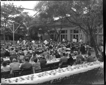 Hundreds of people seated at tables at picnic eating