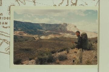 First view of Snyder Mine when crossing from the river opposite 217 Mile Canyon to Trail Canyon.  Harvey Butchart is at right.  The mine is the small white spot in the sun at center
