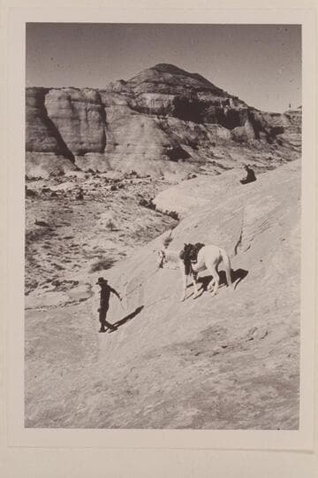 Tobe Owl leads his horse down slick rock on trail into basin north of Butte 5014 which is at top