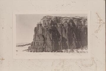 Ten yoke of oxen and four teams of mules freight wagons past the foot of a great sandstone butte on the road from Chinlee to Oljato