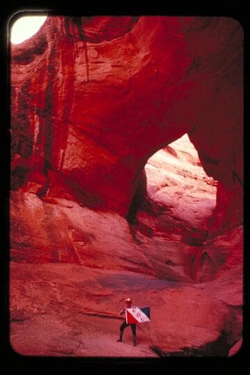 Masland and Marston holding Explorers Club flag at natural bridge in Navajo Canyon.  Masland proposes name, "Ba-Sah Bridge," for the seven pot-holes below it