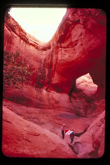 Masland and Marston holding Explorers Club flag at natural bridge in Navajo Canyon.  Masland proposes name, "Ba-Sah Bridge," for the seven pot-holes below it
