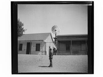 Men next to two wooden buildings, with windmill in background