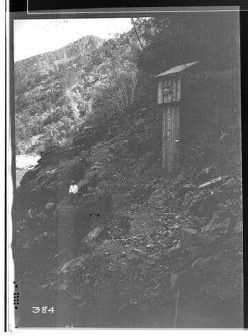 Cabin on a hillside with person sitting on rocks nearby