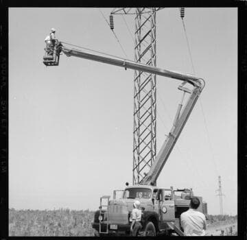 Raising bucket at tower with two men inspecting insulators