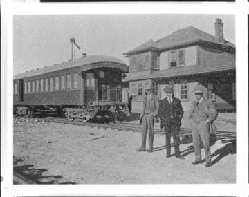 3 men standing by passenger car on track at a RR Station