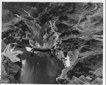 This aerial view shows Hoover Dam, the intake towers, the spillways, and, in the upper right, the electrical substation
