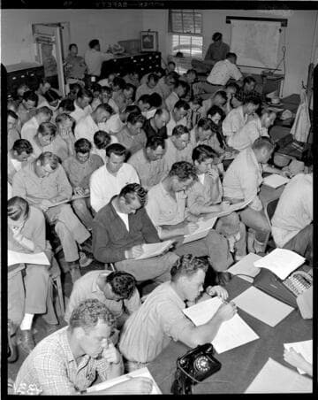 Room full of men filling out "Personnel Survey" forms