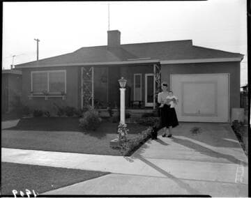 Lady holding baby standing with her dog in her driveway