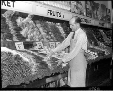 Grocer working with display of produce (rhubarb?) in a market