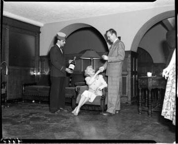 Man with cigar greeting seated woman