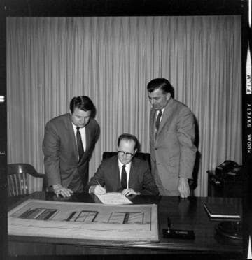 Men in an office setting with an architects drawing of a proposed office building