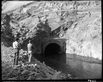 Dam 7 construction work: two men watching water flowing through diversion tunnel